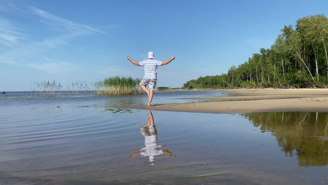 a young man meditates on the beach in summer in the morning, does an asana, a Tree pose.