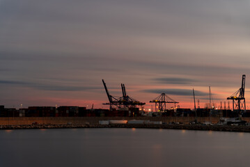 Fototapeta na wymiar Dusk at the bustling commercial port with silhouette of giant cranes