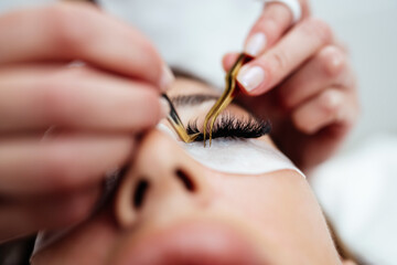 Beautiful young adult woman receiving professional eyelash makeup treatment. Cosmetician is smiling...