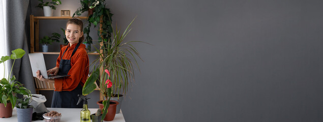Obraz premium Child gardener in green garden uses laptop computer sells houseplants online. Children's small business