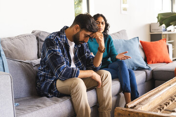Angry biracial couple sitting on sofa and arguing in living room at home