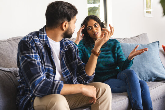 Angry biracial couple sitting on sofa and arguing in living room at home