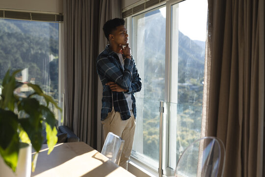 Thoughtful african american man looking out of window in sunny living room, copy space