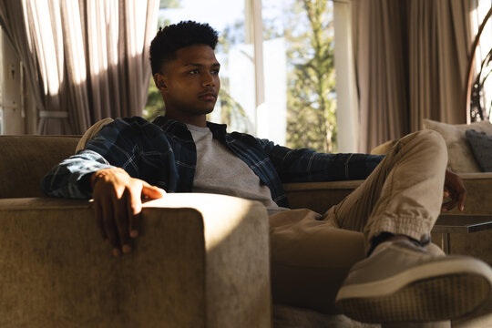 Thoughtful african american man sitting in armchair in sunny living room