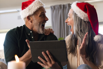 Happy senior caucasian couple sitting on sofa using tablet for christmas video call at home