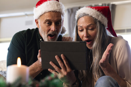 Happy senior caucasian couple sitting on sofa using tablet for christmas video call at home