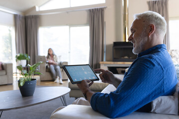 Happy senior caucasian man sitting on sofa using tablet with smart home interface
