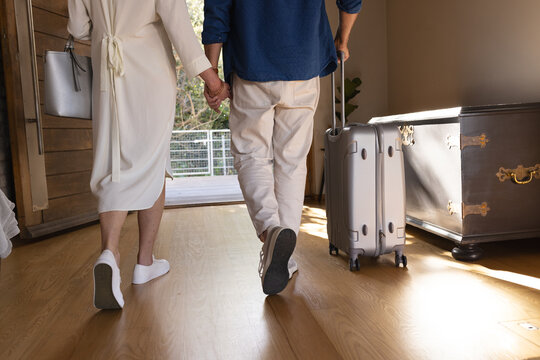 Midsection of senior caucasian couple walking through door with suitcase