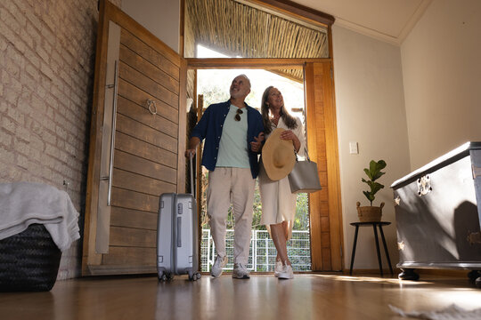 Happy senior caucasian couple walking through door with suitcase