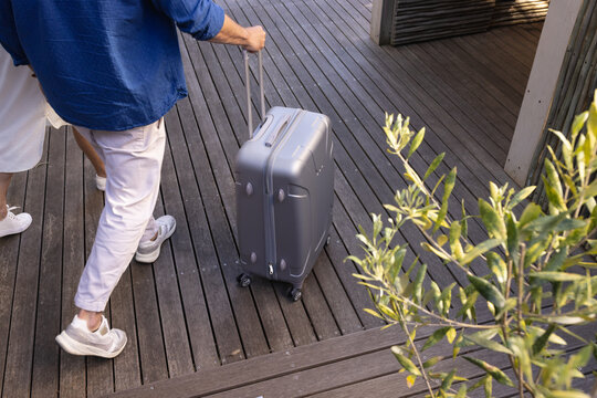 Midsection of senior caucasian couple walking with suitcase