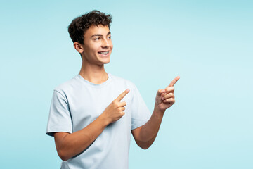 Portrait of confident smiling curly haired school boy pointing finger on copy space isolated on blue background. Education concept