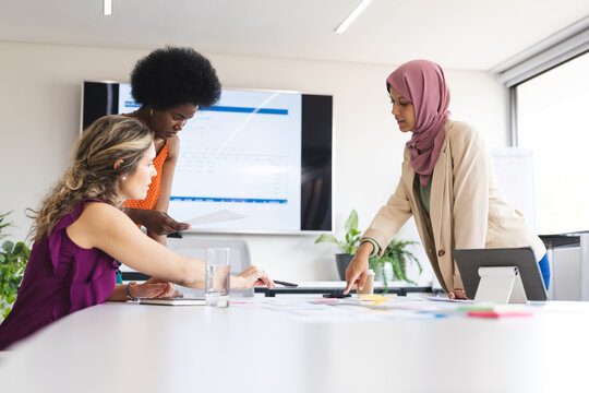 Busy diverse female colleagues at meeting discussing work with documents on table in office