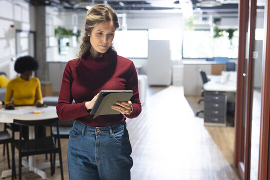 Busy caucasian casual businesswoman using tablet over colleague working in office