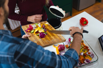 Midsection of caucasian couple preparing food, composting vegetable waste in kitchen