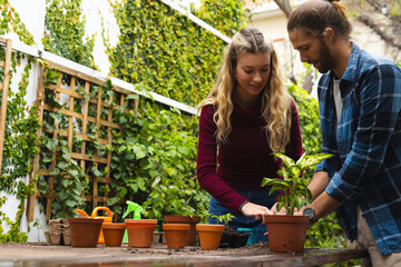 Happy caucasian couple potting plants at table in garden, copy space