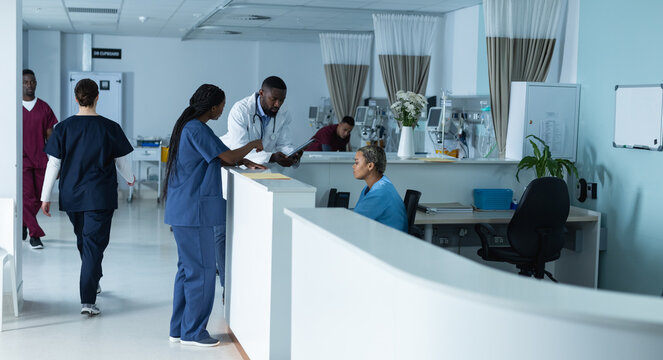 Diverse male and female doctors discussing work, using tablet at reception desk at hospital