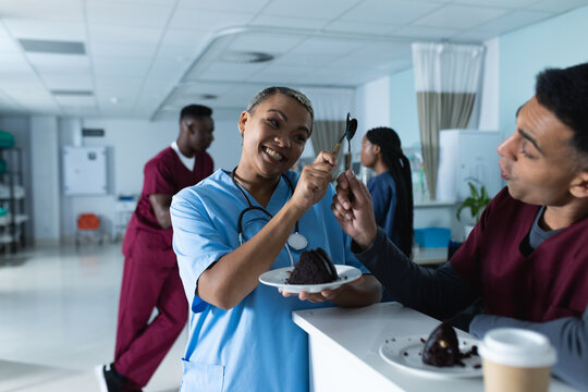 Happy diverse male and female doctors eating birthday cake at reception desk at hospital