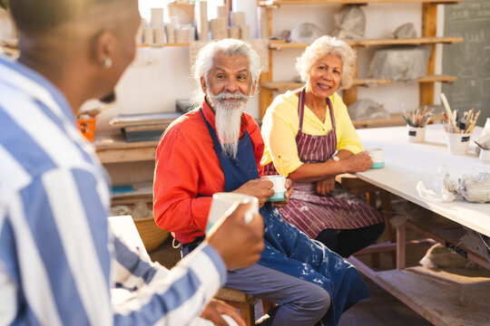 Happy diverse group of potters discussing and smiling in pottery studio - Powered by Adobe