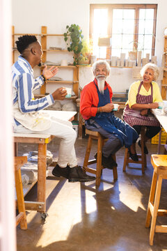 Happy diverse group of potters discussing and smiling in pottery studio