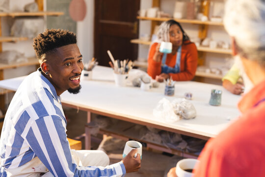 Happy diverse male potters drinking coffee and discussing in pottery studio
