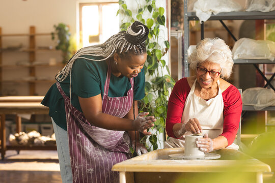 Two diverse female potters working on clay vase using potter's wheel in pottery studio