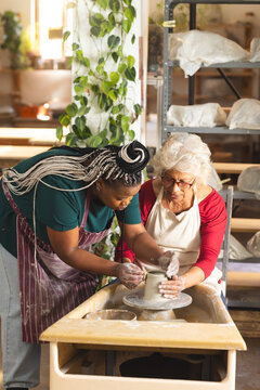 Two diverse female potters working on clay vase using potter's wheel in pottery studio