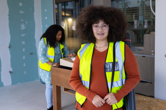 Happy biracial casual businesswoman standing and wearing vest in renovated office, copy space
