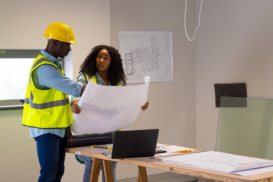 Two african american casual businesspeople discussing over plans in renovated office, copy space
