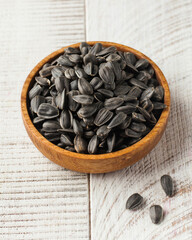 Fried sunflower seeds in a wooden bowl on a white wooden background. Seeds.