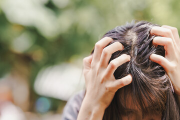 A woman scratches her head where hair is greasy and has fallen out, exposing the scalp.