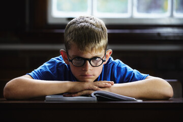 Kid, school and angry on desk, book and staring for education, adhd and child development. Anxiety, stress and burnout from dyslexia, moody or mental health issue for studying, frustrated and autism - obrazy, fototapety, plakaty