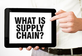 Text WHAT IS SUPPLY CHAIN on tablet display in businessman hands on the white background. Business concept - Powered by Adobe