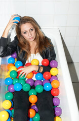 Fototapeta na wymiar Portrait, balls and woman in bathtub for fashion, style and trendy hipster at home. Serious person in tub with color, sphere or plastic with body in bathroom, relax and edgy or cool clothes in Canada