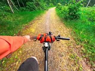 Naklejka premium First-person view of handling the bicycle on the forest road in the city towards sunlight. Concept of using a bicycle for sports and recreation out of a town.