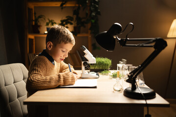 Adolescent pupil looking at sample under the microscope, writing research results, science and education