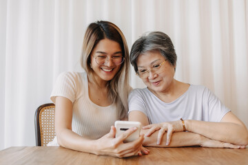 Asian Thai old mother and daughter using phone, both looking at tablet, watching and reading something with happy smiling, spending time together.