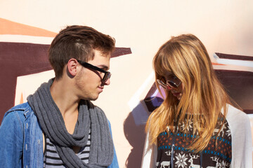 Couple, man and woman with sunglasses for fashion, aesthetic and unique outfit or style outdoor on wall background. People, face and hipster for date, relationship or happiness in urban town or city