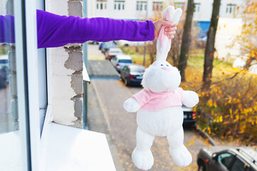 Fototapeta na wymiar On a sunny autumn day, a child throws a toy large white rabbit out of the window.
