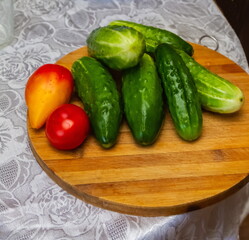 Fresh Cucumbers tomatoes on a wooden kitchen board close-up against a white tablecloth table
