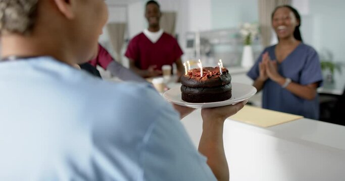 Diverse male and female doctors celebrating birthday at reception desk at hospital, slow motion