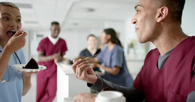 Diverse male and female doctors eating birthday cake at reception desk at hospital, slow motion