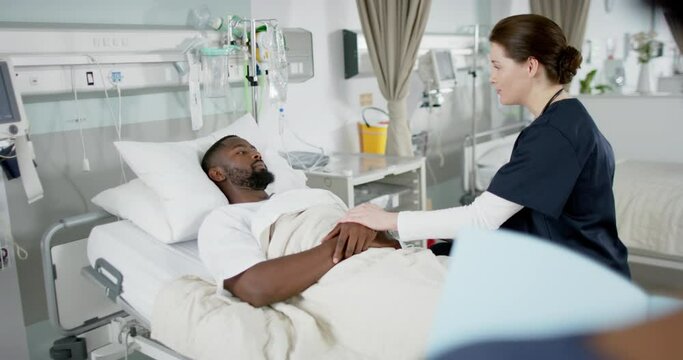 Diverse female doctor and male patient talking in hospital room, slow motion
