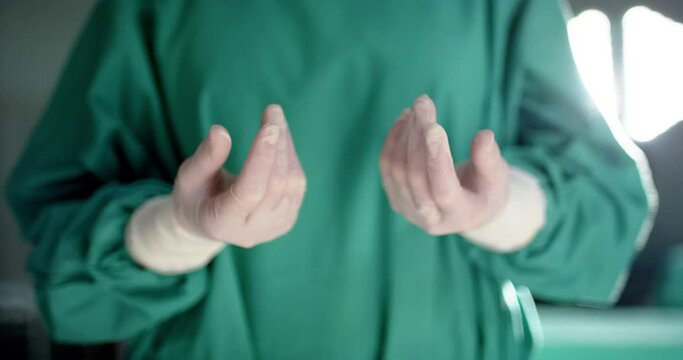 Midsection of caucasian male surgeon wearing medical gloves in operating theatre, slow motion