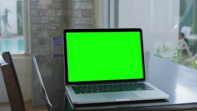 A laptop computer with a key green screen set on work office table. Modern laptop with mock up chroma key green screen on table of living room, desk set up for work at home - technology concept close 