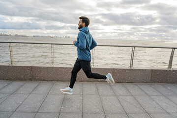 Athlete jogging in warm sportswear for autumn.  Fitness trainer active lifestyle for health. A man runs alone training in the cold.