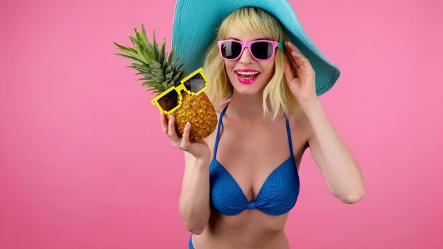 Sexy excited woman in bikini dancing on pink, fashionable hat with pineapple, smiling for spa and wellness. Playful glamor surprised lady dance, slim body for tan or pool party, colorful pink trend