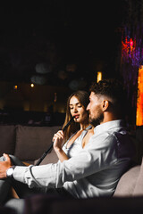 A couple in love drinks a cocktail and smokes a hookah on the terrace at night. Nightlife concept - obrazy, fototapety, plakaty