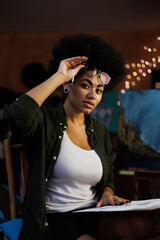 African american artist holding eyeglasses and sketchbook in studio with light
