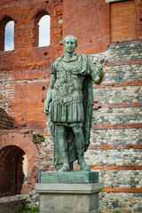 Naklejka premium Turin, Italy. Bronze statue depicting Julius Caesar, in front of the remains of the ancient Porta Palatina, datin gback to Roman times. Vertical image. 2023-05-04.