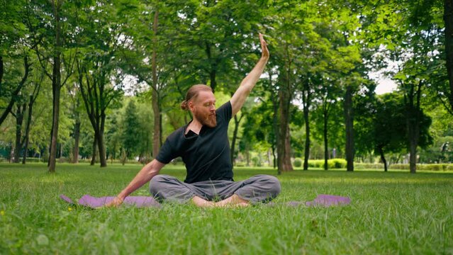 handsome bearded man meditating in the park practicing yoga doing stretching and exercises for different muscle groups
